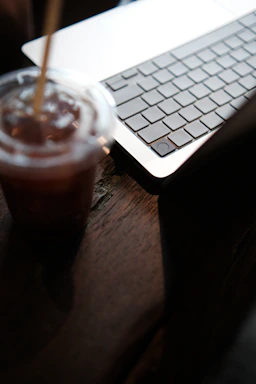 Close-up of hands typing on a laptop keyboard next to a coffee machine.