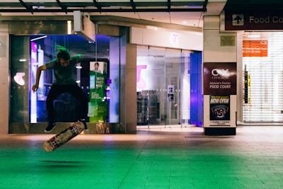 A gritty street corner glowing under neon lights with a silhouetted skateboarder mid-trick.