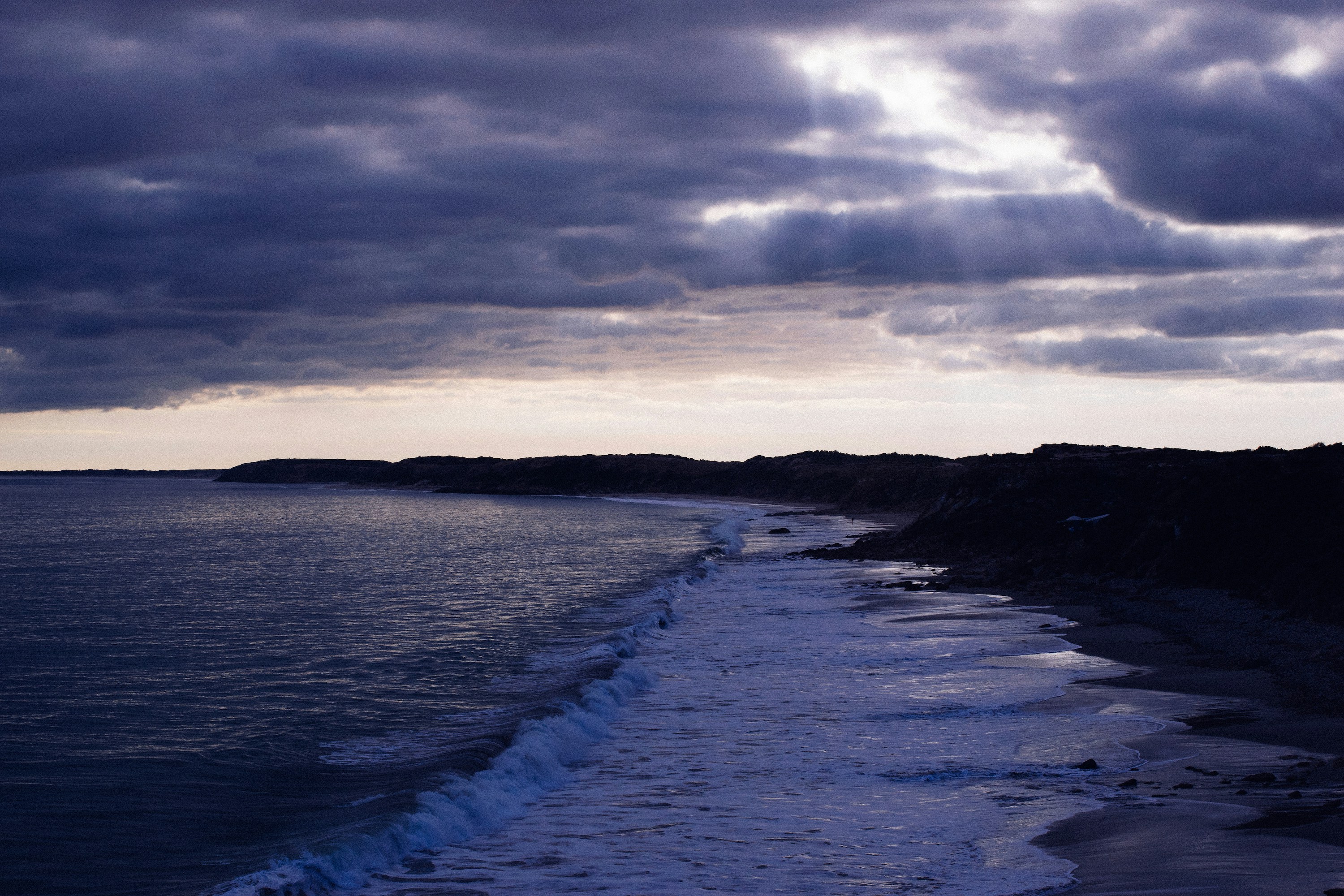 Dramatic coastal seascape with deep navy water, bright sun, crisp maritime atmosphere, moody shoreline