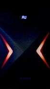 A dark, high-tech speaker with a futuristic design, featuring a prominent X pattern with red and orange lighting accents. Above the X pattern, a digital display shows the letters 'AU' in bright blue.