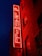 A vibrant red neon sign reading 'The Leadmill' is mounted on the brick exterior of a building. The sign glows against the dark blue night sky, creating a striking contrast. The building features several windows with darkened glass.