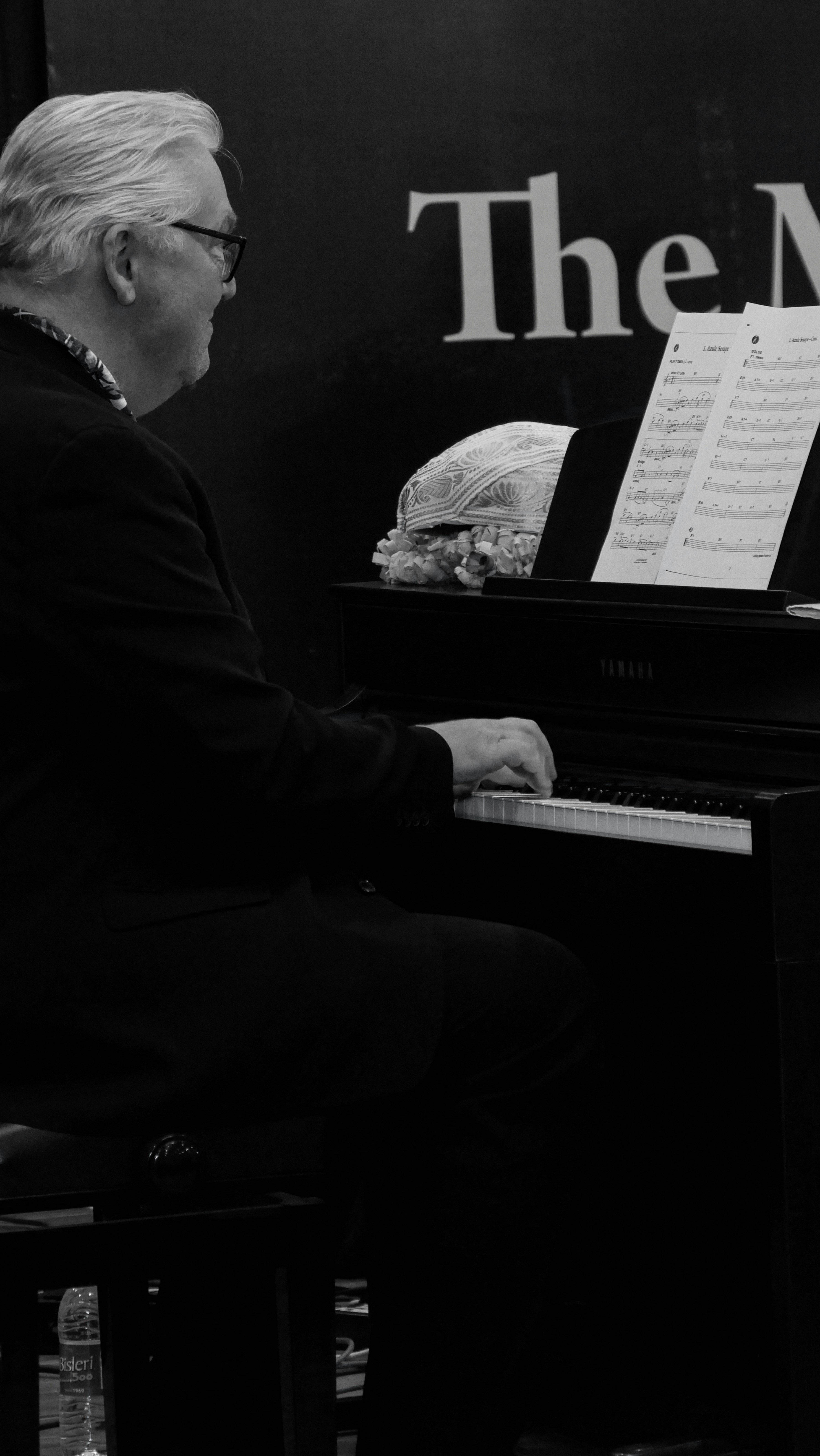 Un hombre sentado frente a un piano frente a un letrero