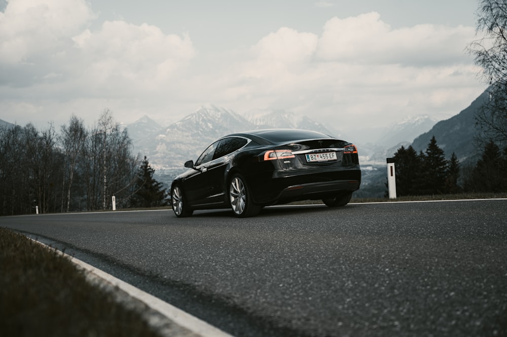 a black car driving down a road next to a forest