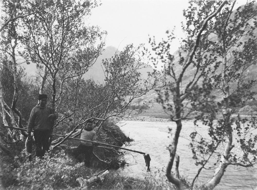 a black and white photo of a man standing next to a river