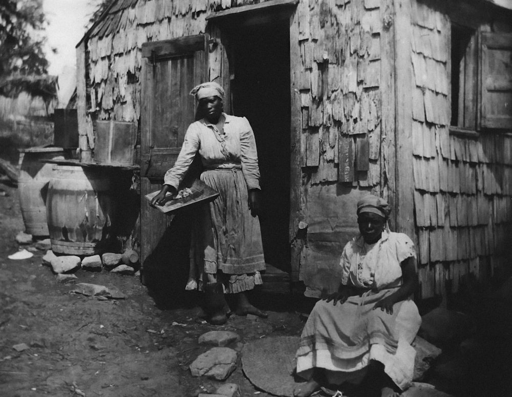 an old black and white photo of two women in front of a shack