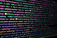 The image features colorful lines of code on a computer screen, showcasing various syntax elements with different colors to highlight keywords, values, and functions. The background is dark, enhancing the visibility of the text.
