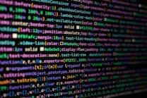 The image features colorful lines of code on a computer screen, showcasing various syntax elements with different colors to highlight keywords, values, and functions. The background is dark, enhancing the visibility of the text.