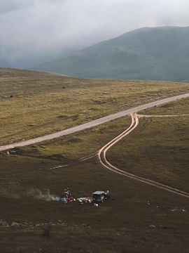 A rugged campsite at dawn with a tent, campfire, and gear laid out on a tarp