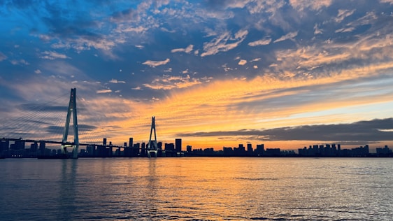 A panoramic view of a massive cable-stayed bridge under construction against a vibrant sunset sky.