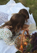 two young girls sitting on a blanket reading a book