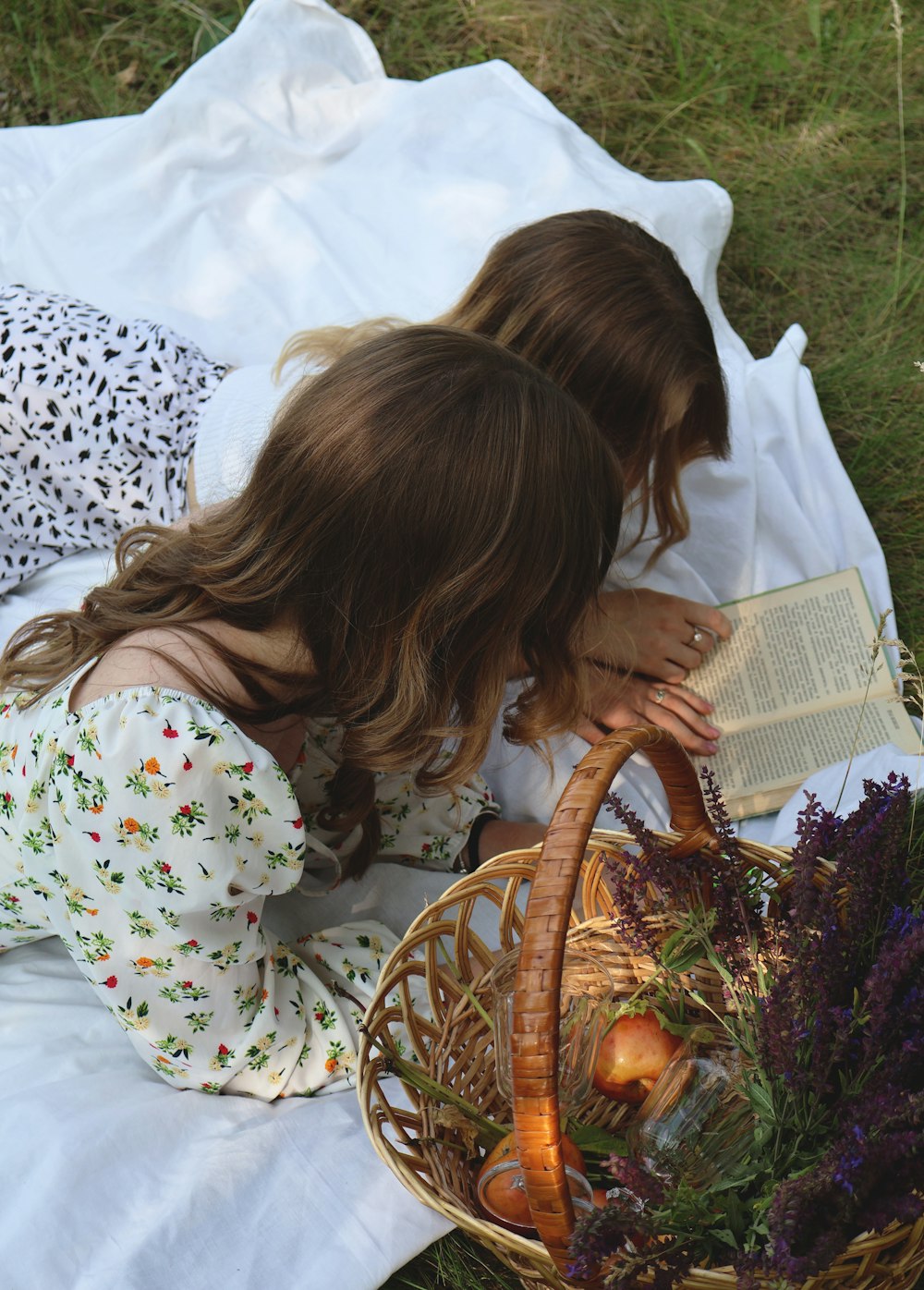 two young girls sitting on a blanket reading a book