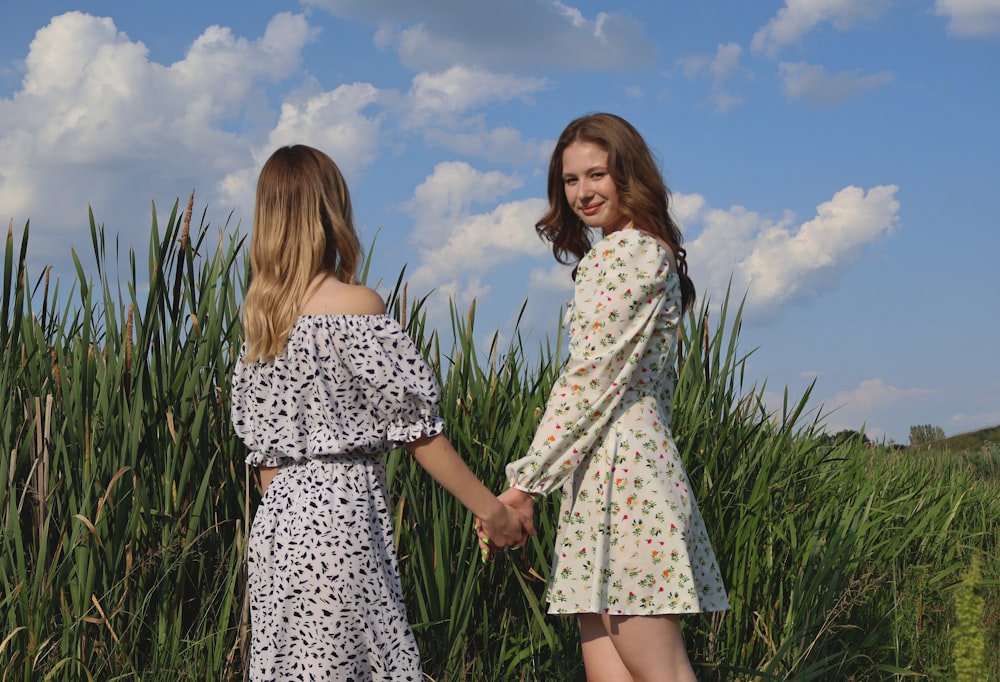 two women holding hands in front of a field of tall grass