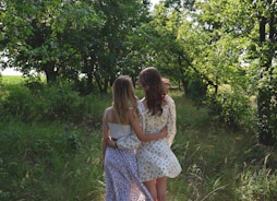 two girls are walking down a path in the woods