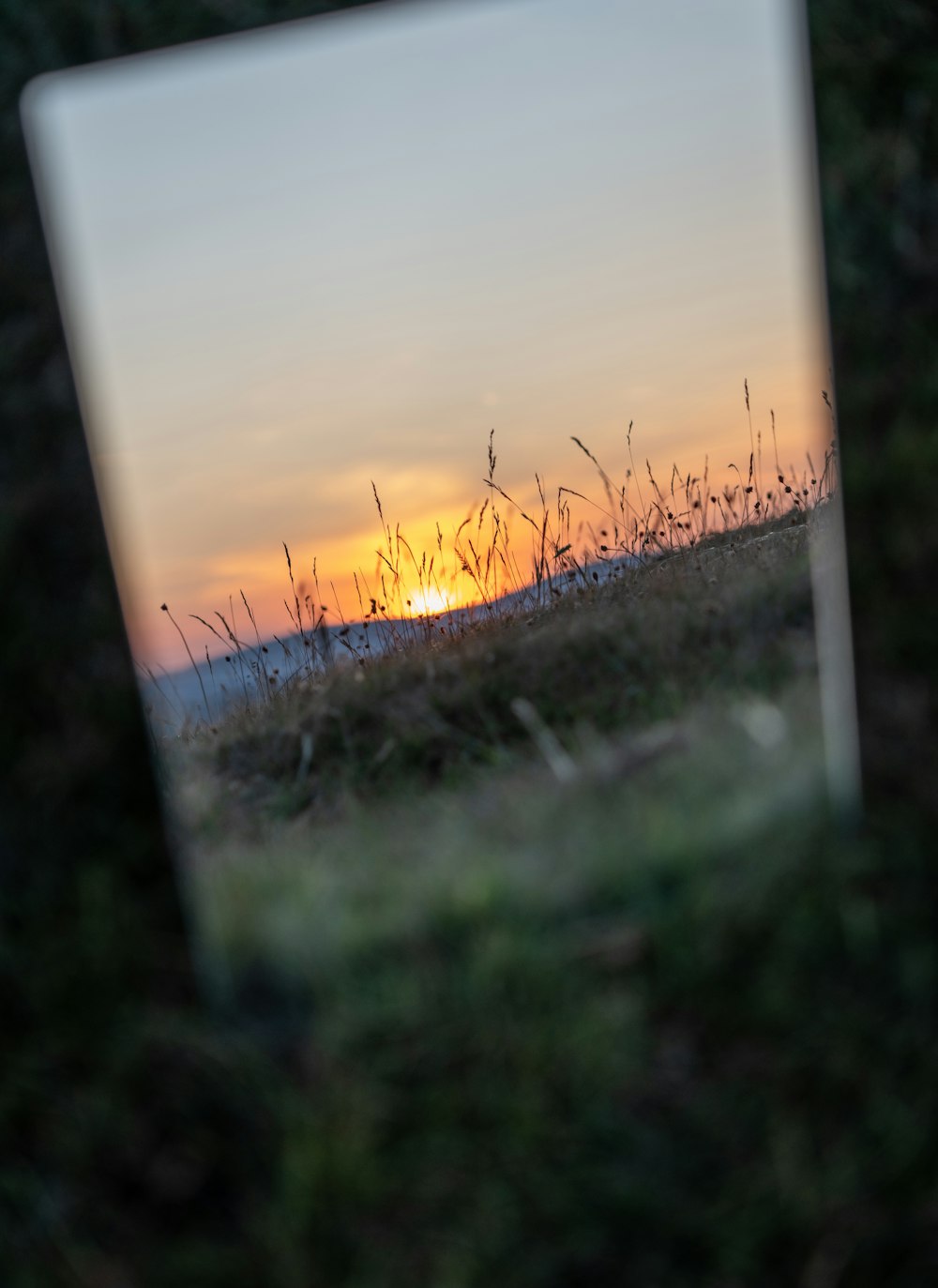 a mirror reflecting a sunset in a grassy field
