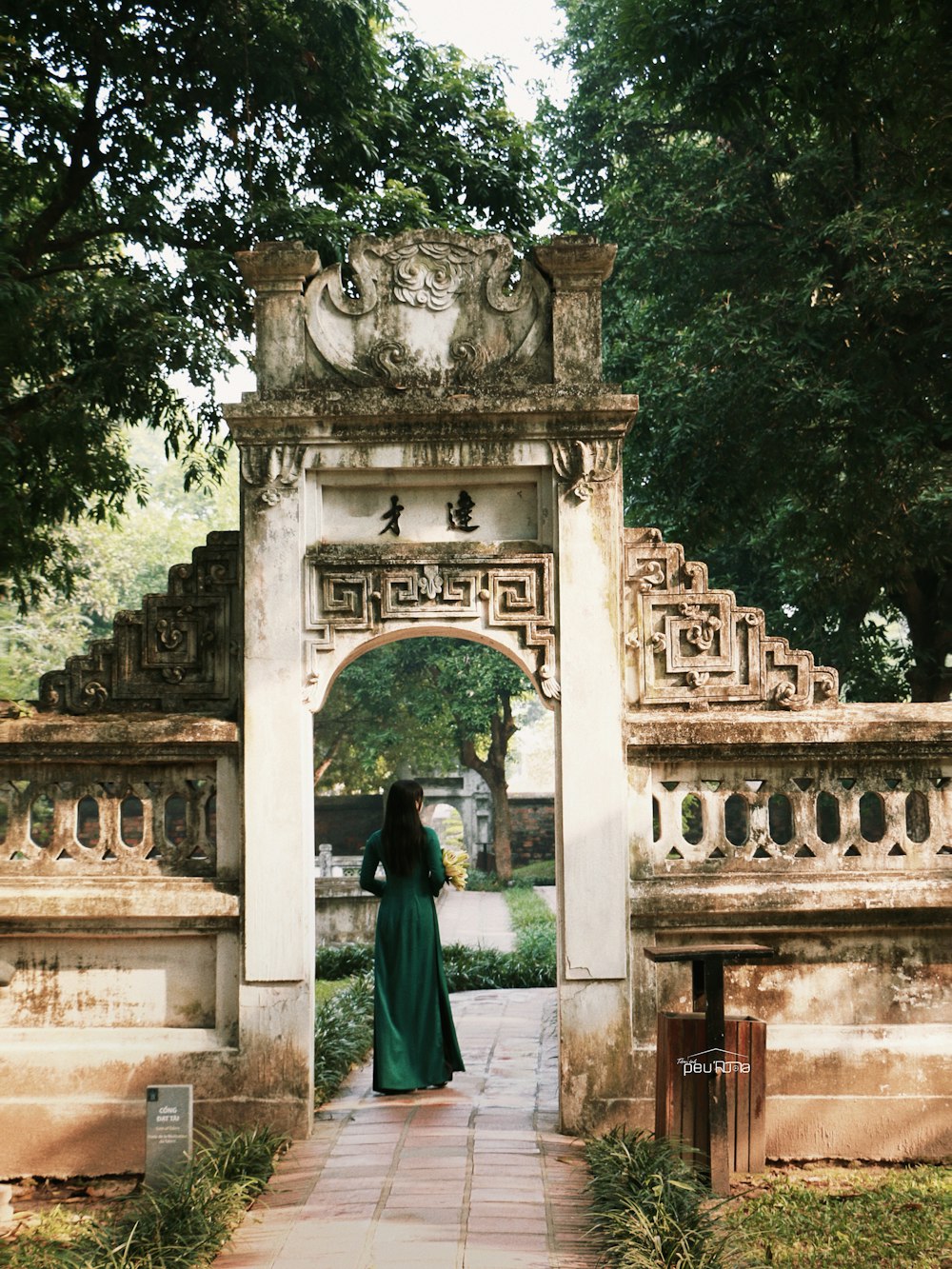 a woman in a long green dress standing in front of a gate