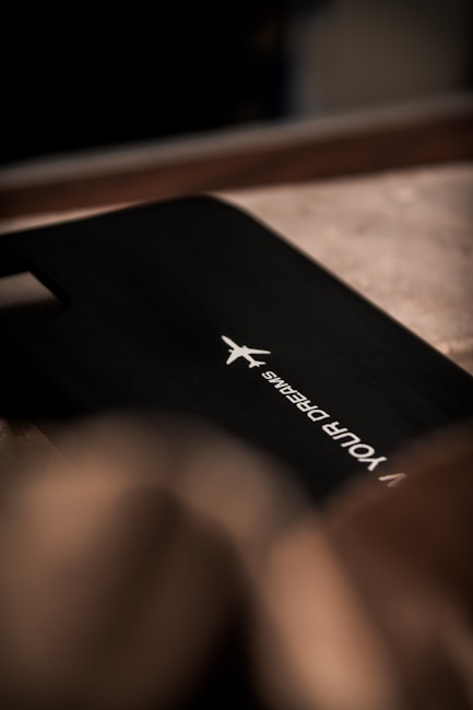 A sleek black surface with a white airplane logo and the words 'YOUR DREAMS' printed in a minimalist font. The lighting is dim, creating a subtle play of shadows on the textured background.