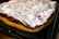 A baking tray holds a partially baked dessert featuring a thick layer of golden brown dough topped with fluffy white cream or meringue. The white cream has streaks of red filling visible underneath, adding a contrasting color and texture.
