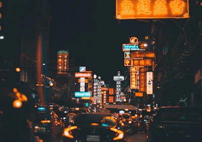 A bustling city street at night illuminated by neon signs and passing cars.