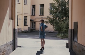 A model wearing a flowing, pastel-colored dress standing in a sunlit urban courtyard.
