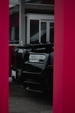 A luxurious black car is partially visible, framed by red pillars, with large glass windows and a modern building facade in the background.