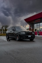 A sleek black luxury SUV parked in front of a modern airport terminal at sunset.
