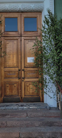 A set of double wooden doors painted in bold colors, framed by lush greenery.