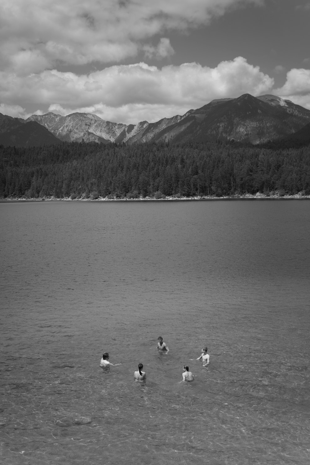 a group of people wading in a lake with mountains in the background