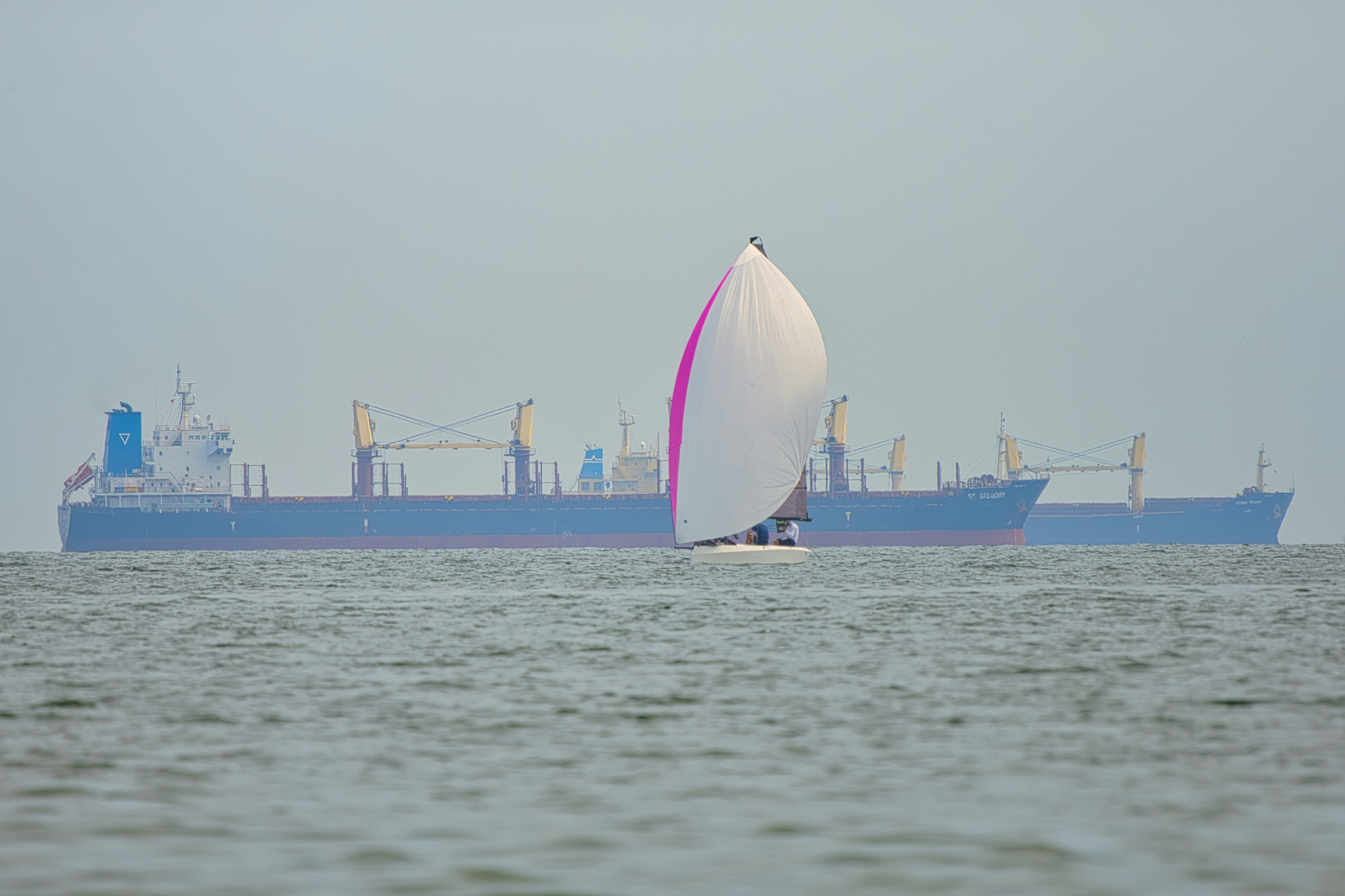 a sailboat with a large cargo ship in the background
