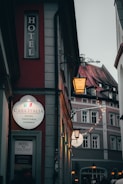 A narrow street featuring a building with a bright sign for Casa Italia, a hotel and pizzeria. The area is dimly lit, with ambient lighting from street lamps, creating a cozy atmosphere. Adjacent buildings show classic architecture with decorative facades.