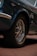 A close-up of a vintage car's front tire and wheel, featuring chrome details and radial tires with 'BFGoodrich' branding. The car is parked on a brick surface, and part of the blue metallic body with chrome trimming is visible.