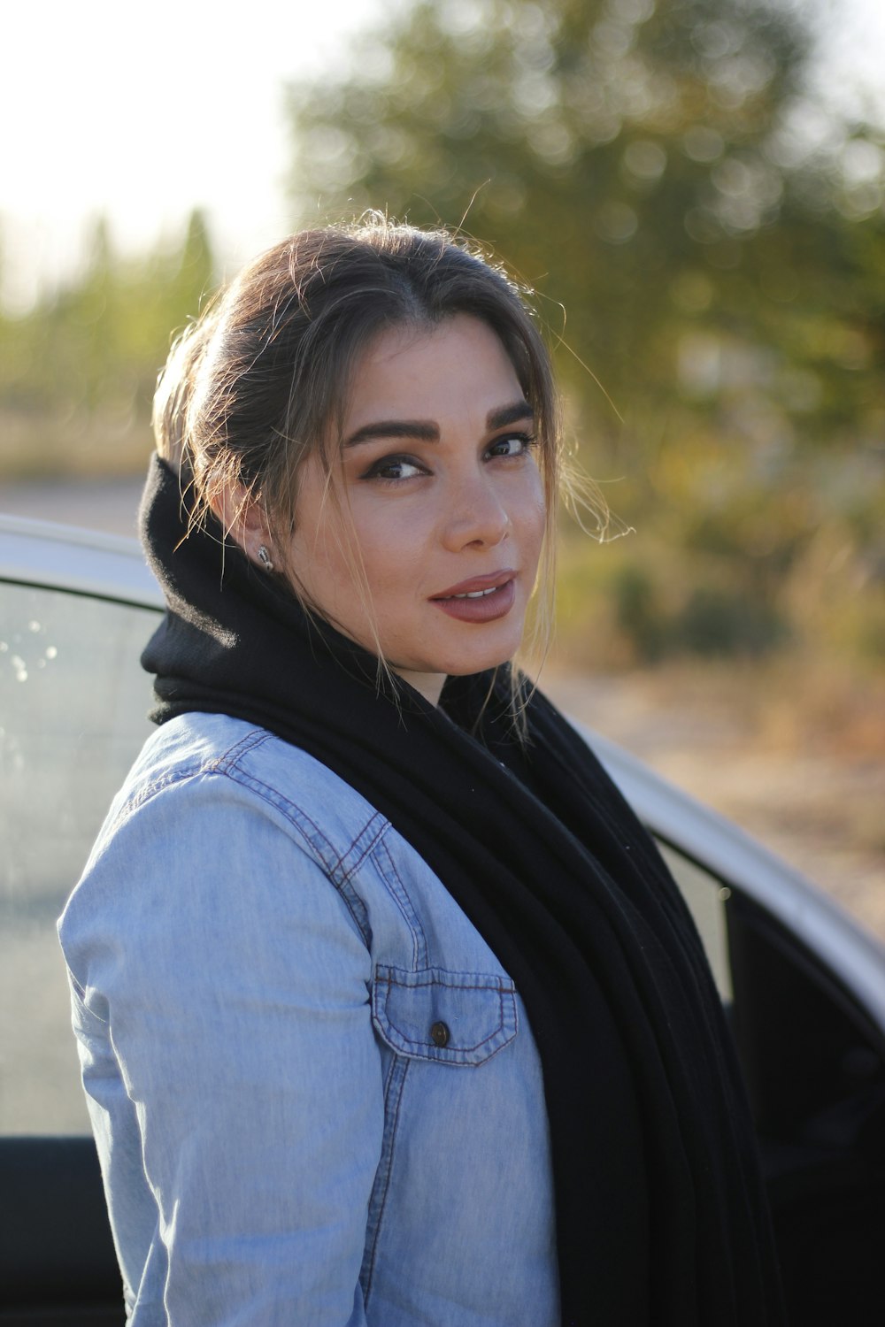 a woman standing next to a car wearing a scarf