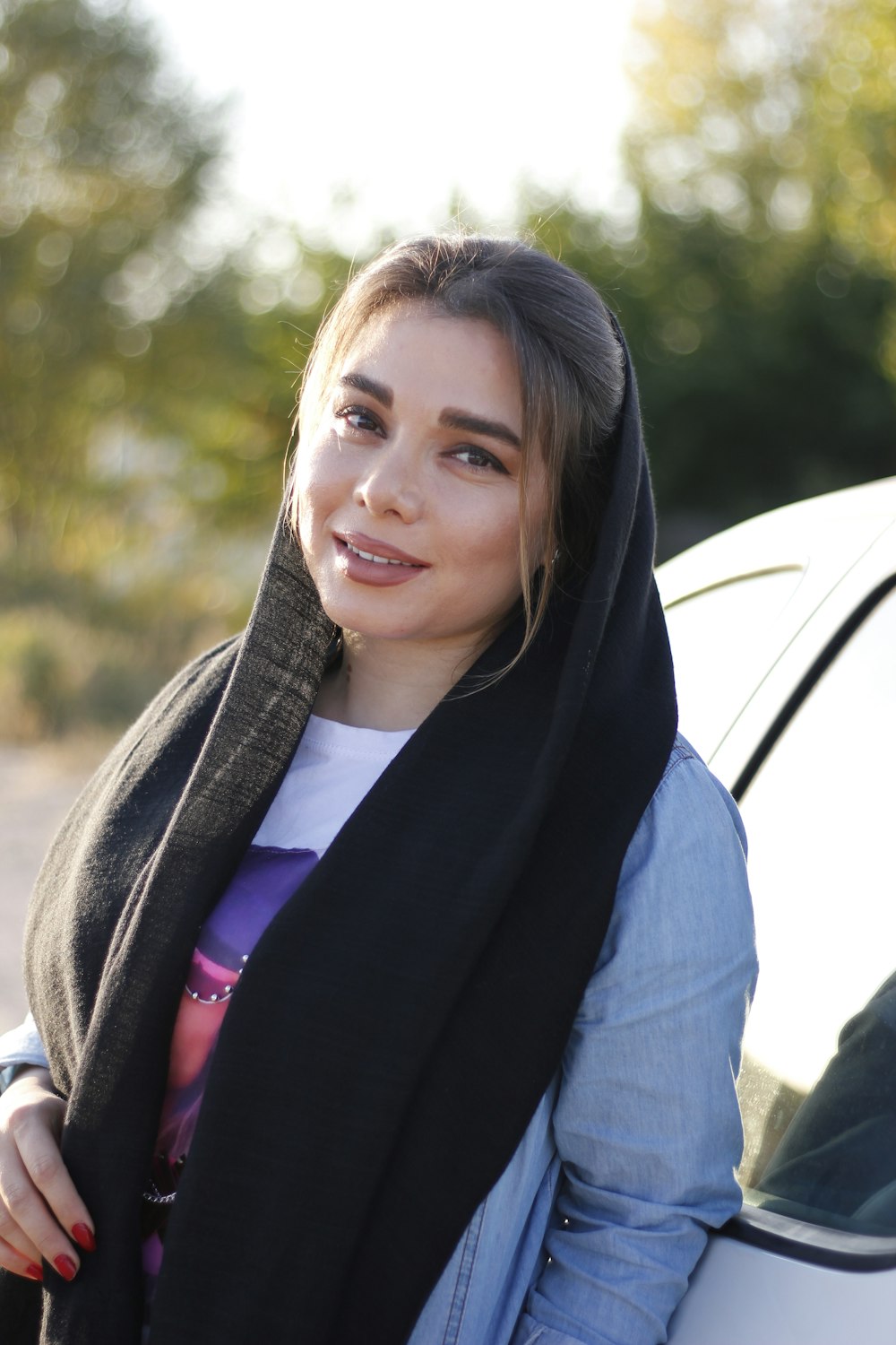 a woman wearing a scarf standing next to a car