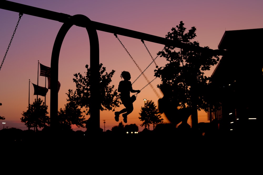 a silhouette of a child swinging on a swing set