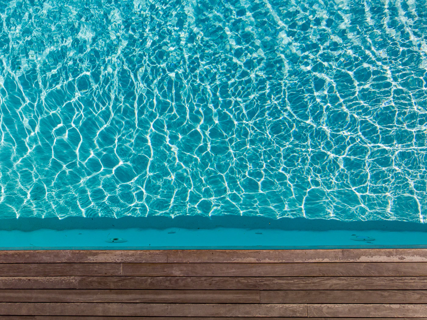 An aerial view of a turquoise swimming pool bordered by a wooden deck