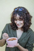 A smiling person holding a freshly glazed ceramic bowl against a soft pastel background.