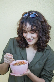 Happy person holding a colorful bowl of healthy dessert in a bright kitchen.