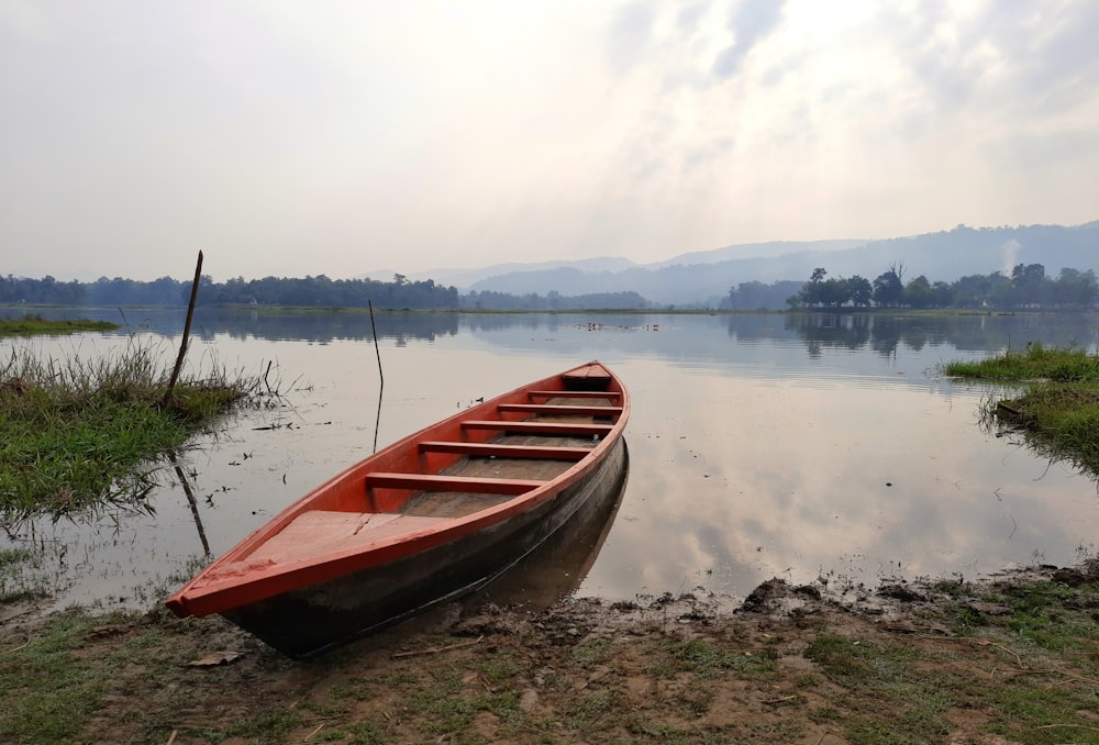 a red canoe sitting on the shore of a lake