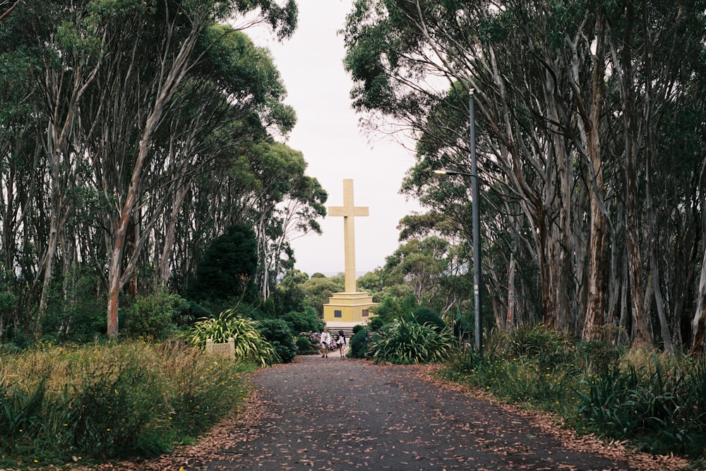 a cross in the middle of a road surrounded by trees