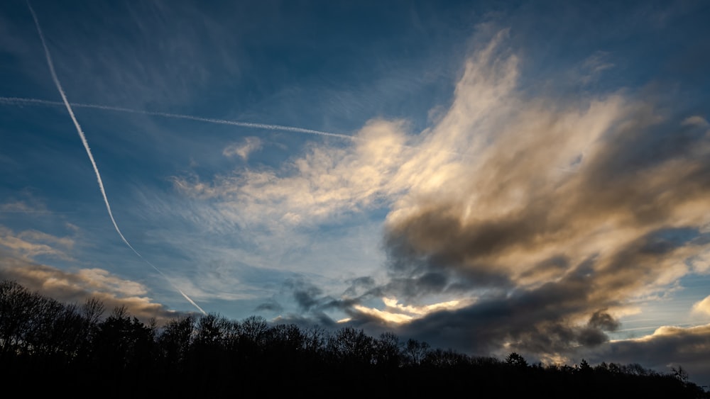 a cloudy sky with contrails in the distance