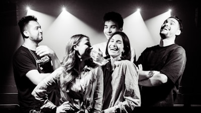 A lively group of colleagues laughing and acting out a scene in a bright, theatrical workshop space.