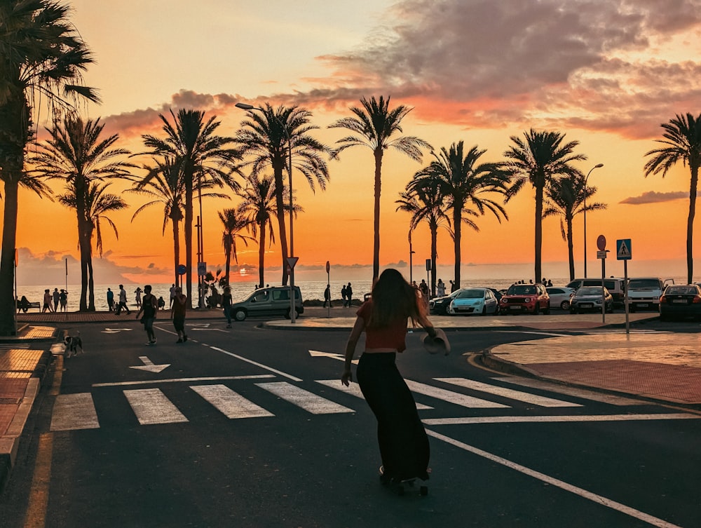 a woman riding a skateboard down a street next to palm trees