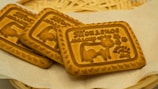 Three rectangular biscuits with embossed designs, featuring a cow, decorative patterns, and Cyrillic script. They are placed on a light napkin with a woven basket in the background.