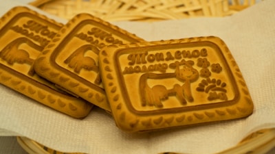 Three rectangular biscuits with embossed designs, featuring a cow, decorative patterns, and Cyrillic script. They are placed on a light napkin with a woven basket in the background.