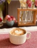 A vibrant latte art heart on a creamy coffee surface, set against a pink tablecloth.