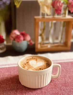 A vibrant latte art heart on a creamy coffee surface, set against a pink tablecloth.