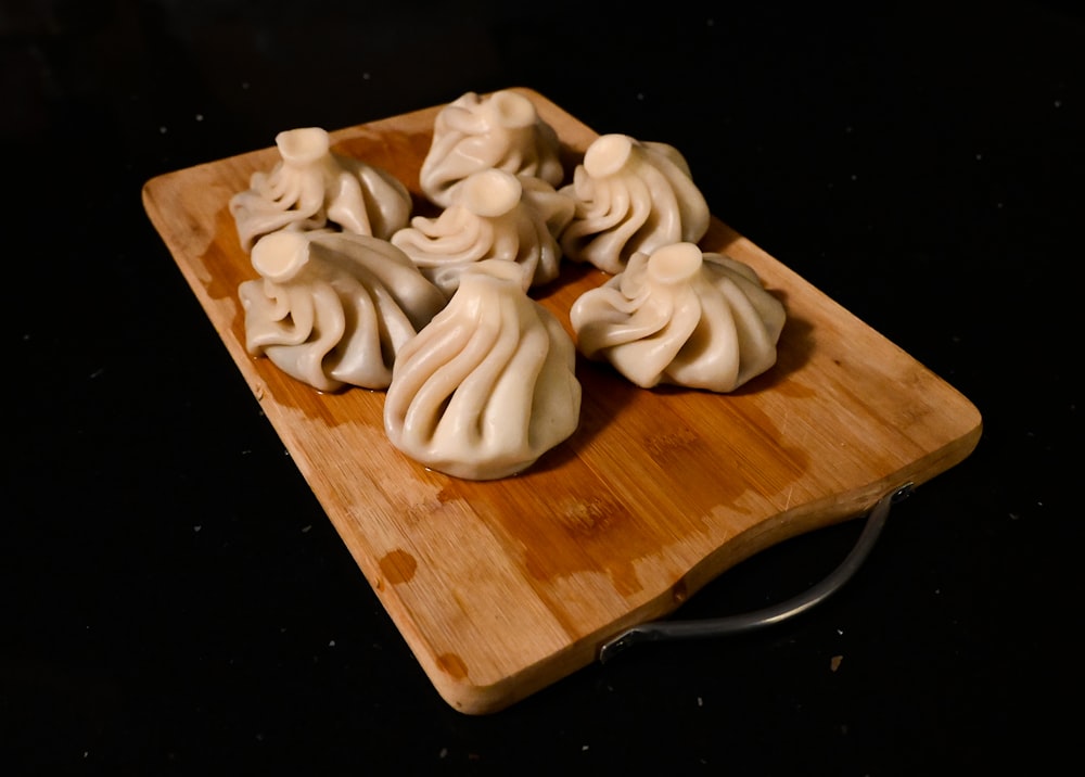 a wooden cutting board topped with dumplings on top of a table
