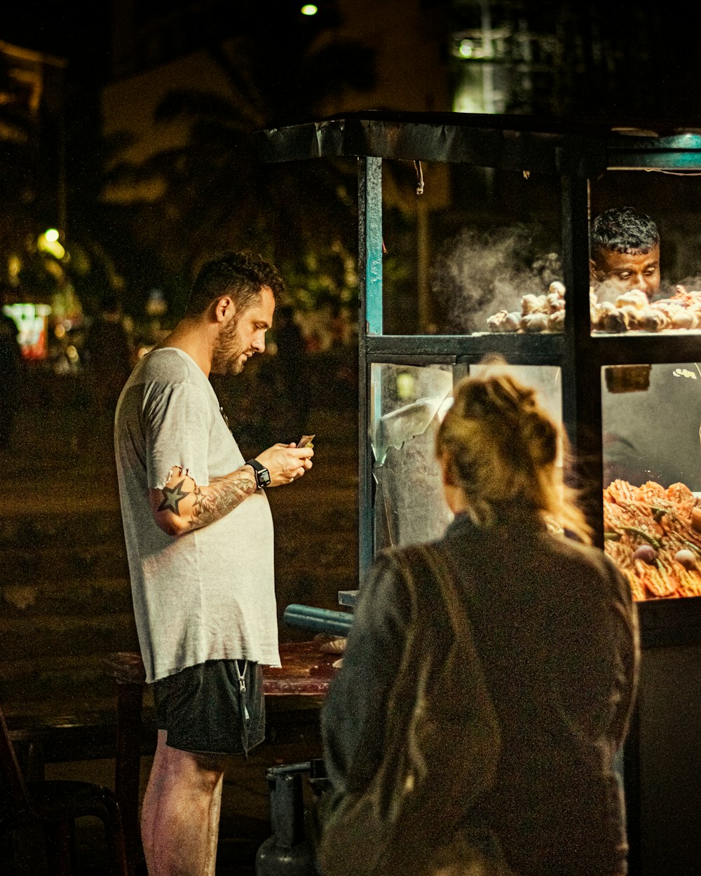 a man standing next to a woman in front of a food cart