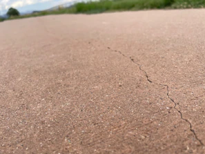 Technician carefully inspecting a residential concrete driveway for cracks.