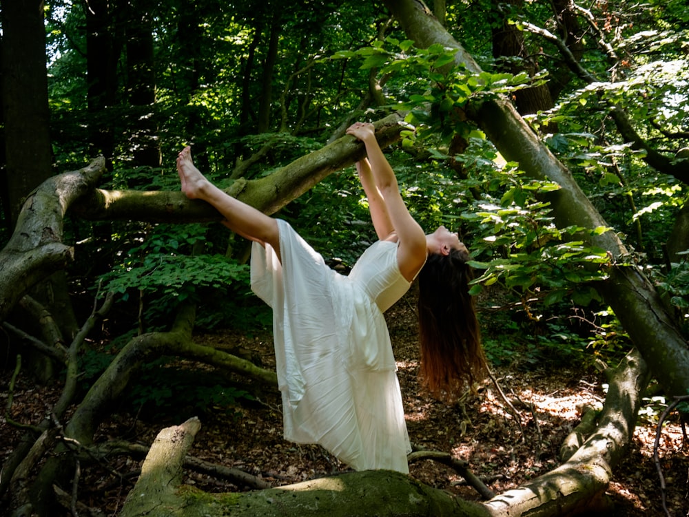 una mujer con un vestido blanco de pie en una rama en el bosque