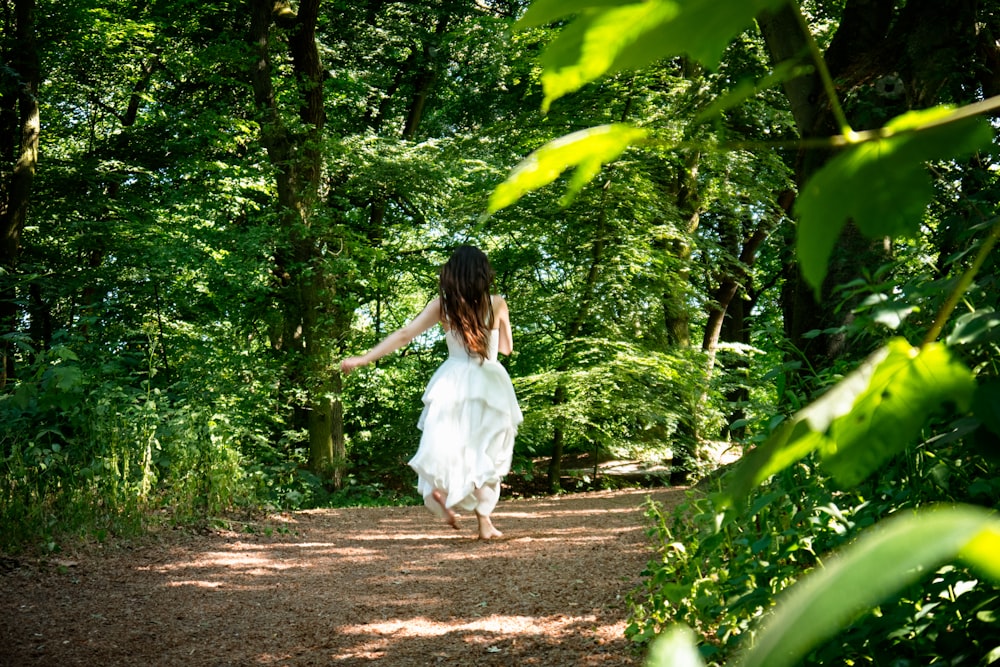 a woman in a white dress is walking through the woods